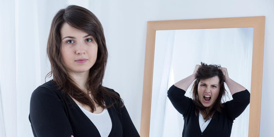 Image d'une femme impassible avec son reflet en colère dans un miroir pour illustrer l'importance de l'observation de soi pour détecter les mécanismes de défense.